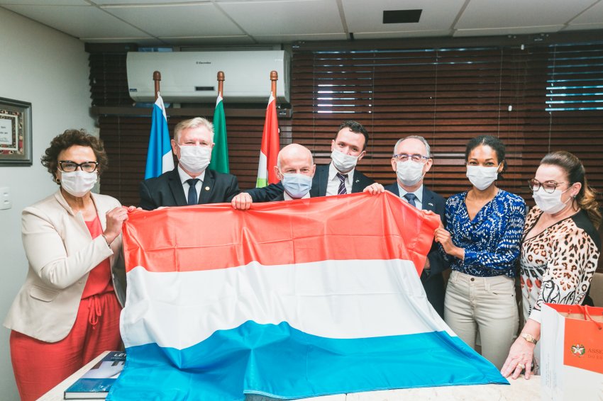 Deputados e membros da embaixada seguram a bandeira de Luxemburgo